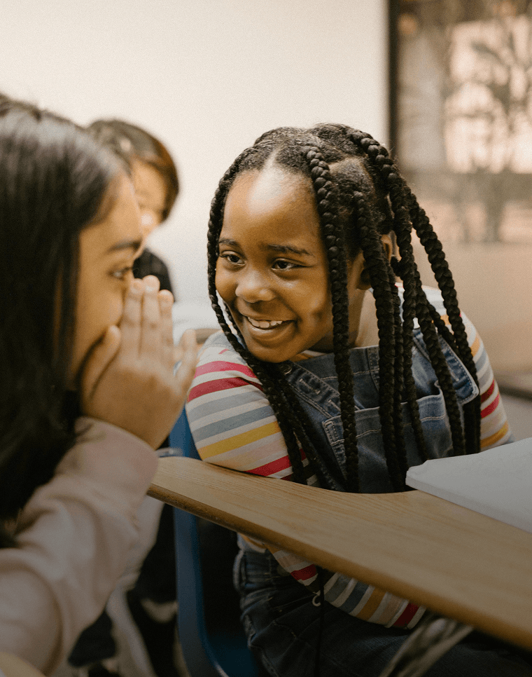 Alunos sorridentes sussurram uns aos outros enquanto aprendem um novo idioma na escola.